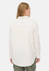 Lange mouwen, crèmekleurig shirt met een kraag, achterpand detail en knoopmanchetten. Zachte stof met een ontspannen pasvorm en ronde zoom.