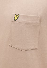 Beige katoenen t-shirt met een borstzakje waarop een geel geborduurd logo staat. Soepele textuur, casual ontwerp en standaard pasvorm.