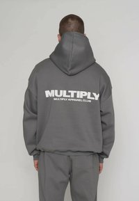 Sudadera con capucha gris que presenta un gran logo blanco impreso en la espalda. El diseño incluye una capucha espaciosa y un ajuste relajado con textura suave.