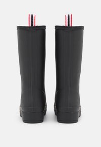 Bottes de pluie en caoutchouc noir avec une finition texturée, deux anses arrières avec des rayures rouges et noires, et une semelle plate robuste.