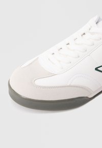 Cipela s gornjim dijelom od bijele kože s sivim detaljima od brušene kože, okruglim vrhom, ravnim vezicama i gumenim potplatom sa blagom teksturom.