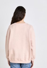 Zachte roze sweatshirt met een gecombineerde, gestructureerde afwerking. Loose fit, ronde halslijn en geribbelde manchetten en zoom. Ggedragen met blauwe jeans.