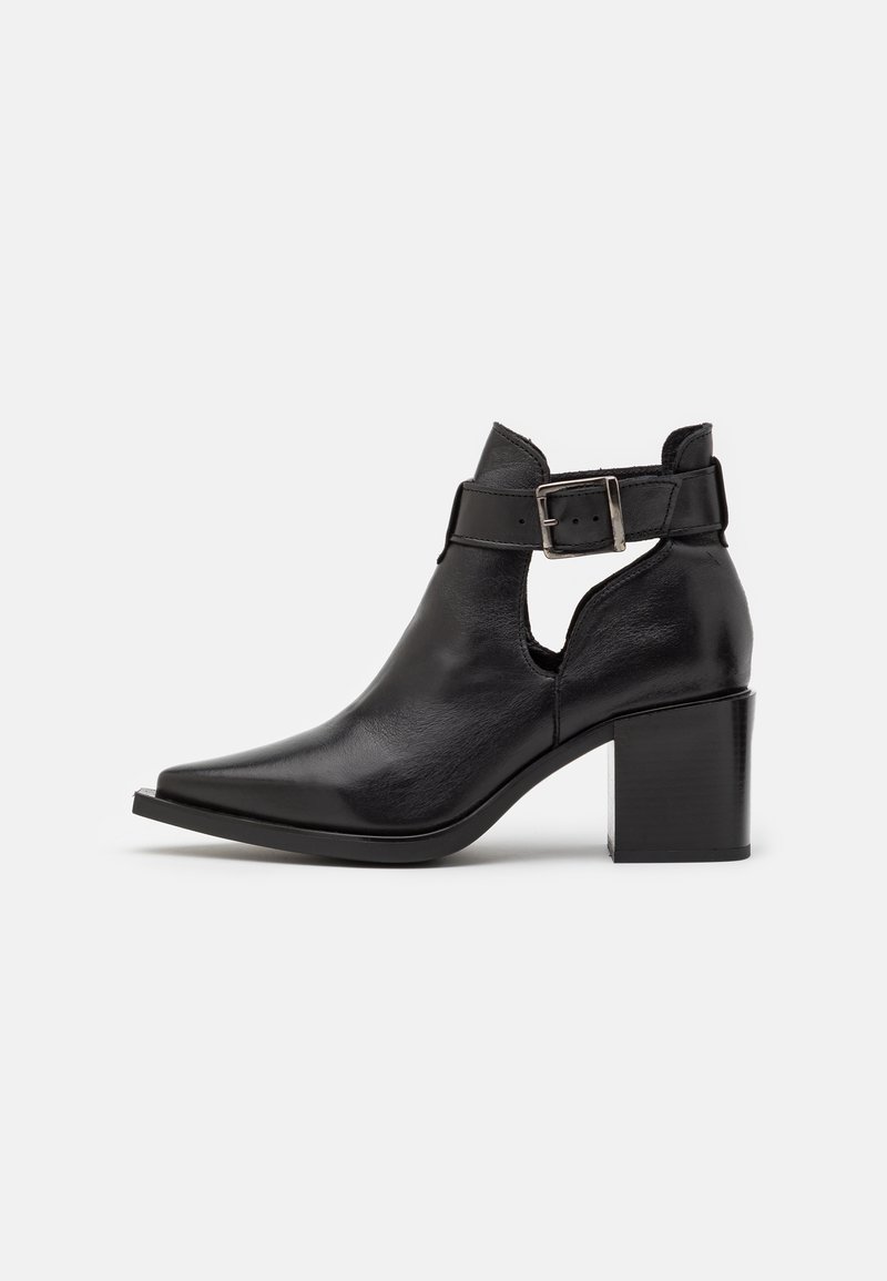 Bottine en cuir noir avec bout pointu, talon bloc, côté découpé et bride ajustable avec boucle argentée.