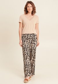 Beige v-hals t-shirt gecombineerd met zwarte broeken met een beige en perzikbladpatroon; model draagt tan espadrille sandaaltjes.