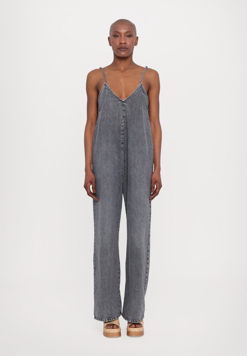 Salopette en denim gris avec des bretelles fines ajustables, un décolleté en V profond et une coupe large. Présente des surpiqûres le long du col.