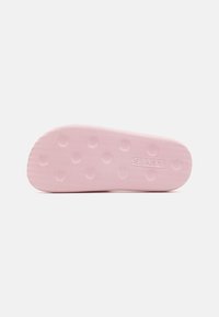 Pink gummiskoled med en tekstureret overflade, der har små, cirkulære greb og et debosseret logo. Glatte kanter med en let krumning.