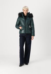 Dark green puffer jacket with a detachable black fur hood. Features a zip closure and angled quilted pattern. Paired with dark wide-leg jeans.