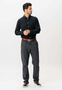 Sort skjorte med knap-up, grå tapered bukser, brun bælte og mørke sko; skjorten har en krave og en glat stofstruktur.