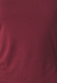 Top fitted bordeaux realizzato in cotone a costine, con una texture liscia e un classico collo a giro senza loghi o motivi visibili.