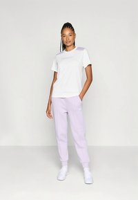 Biała bawełniana koszulka z liliowym akcentem na ramieniu oraz liliowe spodnie dresowe z elastyczną talią i mankietami. Białe trampki.