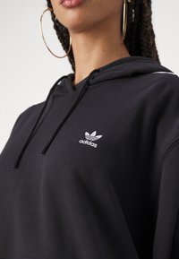 Sudadera negra de algodón con capucha y cordón ajustable. Presenta un logo de Adidas bordado en blanco en el lado izquierdo del pecho. Tejido texturizado.