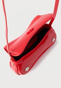 Spīdīga sarkana plecu soma ar atvērtu pārsegu, magnētisku aizdari un melnu iekšpuses oderi uz baltas fona.