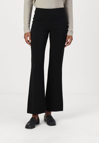 Svarta utsvängda byxor med hög midja, slät textur och vida ben, i kombination med svarta loafers. Tyget ser ut att vara stretchigt och mångsidigt.