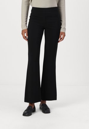 Schwarze, weit ausgestellte Hose mit hohem Bund, glatter Textur und weitem Bein, kombiniert mit schwarzen Slippers. Der Stoff scheint dehnbar und vielseitig zu sein.