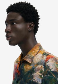 Camicia floreale multicolore con colletto strutturato, caratterizzata da tonalità vivaci di arancione, verde e motivi bianchi su un tessuto morbido.