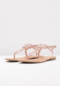 Litte sandaalit, joissa on ruusukultaiset punottu hihna, varpaiden väli ja nilkkahihna vaalean beigen pohjan päällä. Sileä rakenne.