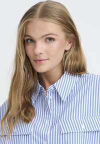 Blue and white striped button-up shirt with a collar, featuring two chest pockets and a smooth cotton texture.