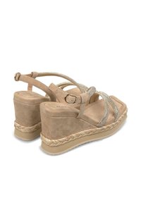 Wedge sandals featuring a beige suede material, sparkling silver straps, and a braided rope accent along the sole. Adjustable ankle buckle.