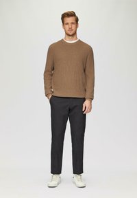 Bruin gestructureerd brei-sweater, zwarte broek en witte sneakers. De outfit heeft een ronde hals en een casual silhouet. Neutrale kleurenpalet.