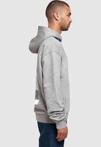 Grå hættebluse lavet af blødt materiale, med en afslappet pasform, frontlomme i kangaroo-stil og elastiske manchetter. Minimalistisk design.