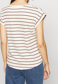 T-shirt crème à rayures avec des manches courtes retroussées et une coupe décontractée, arborant des rayures horizontales marron foncé et un ourlet arrondi.