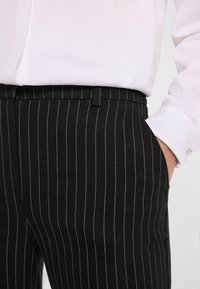 Czarne spodnie w srebrne paski z białymi pionowymi liniami, dopasowany krój i gładka faktura. W komplecie z elegancką białą koszulą.