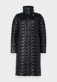 Chaqueta tipo puffer negra con cuello alto y diseño acolchado en forma de ondas. Presenta una textura elegante y brillante, con un diseño de largo hasta la mitad de la pantorrilla.