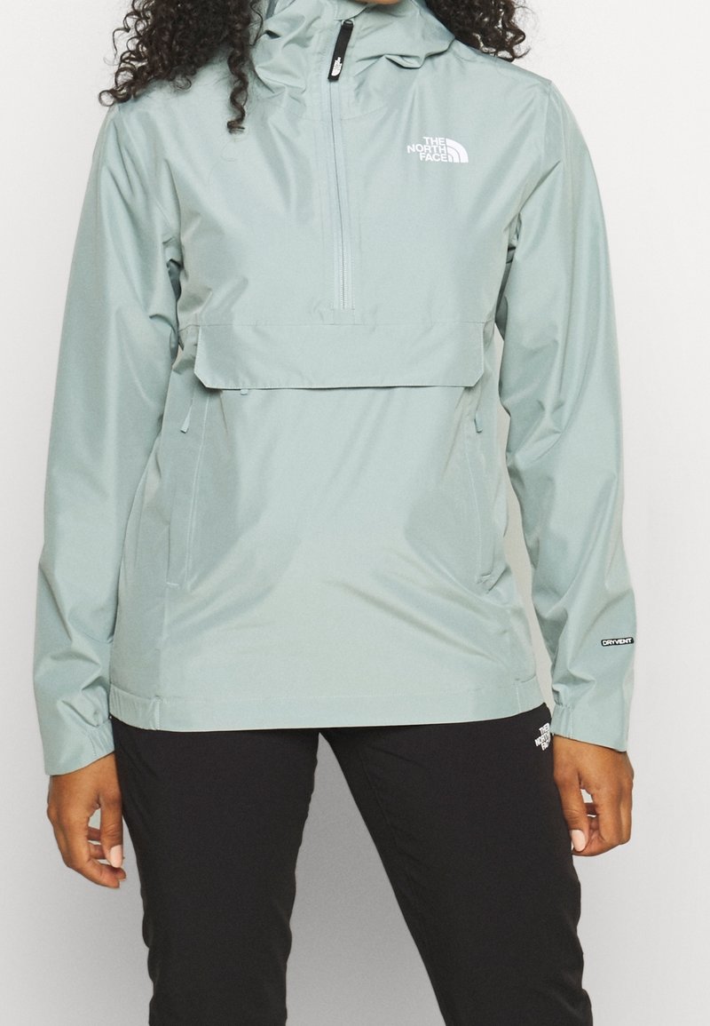 Light green pullover jacket with a half-zip front, adjustable hood, and front pocket. Smooth, water-resistant fabric with logo accents.