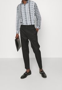 Camicia a maniche lunghe bianca e nera con colletto, abbinata a pantaloni neri a sigaretta. Scarpe scure e una pochette nera completano l'outfit.