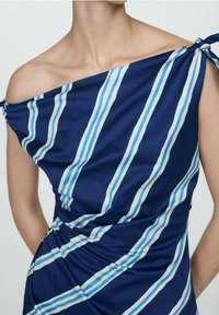 Robe bleu marine à rayures bleues et blanches, design épaules dénudées, détail noué sur un côté, tissu lisse avec un aspect drapé et une légère brillance.
