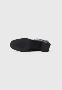 Zapato de cuero negro, con tacón bajo y cuadrado, suela texturizada visible, acostado de lado sobre un fondo blanco.