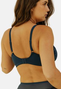 Soutien-gorge bleu marine avec bretelles réglables, en tissu lisse, fermeture à crochets et détails en dentelle à l'avant. Aucun rembourrage n'est visible dans le design.