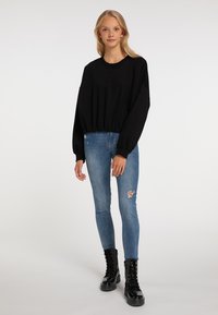 Felpa nera corta con maniche lunghe, abbinata a jeans skinny azzurri chiari con un ginocchio strappato. Stivali combat neri con lacci.