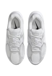 Balts Nike skriešanas apavu pāris ar acs virsējām daļām, sasietām šņorēm un melniem Nike logotipiem zoles iekšpusē, redzams no augšas uz balta fona.