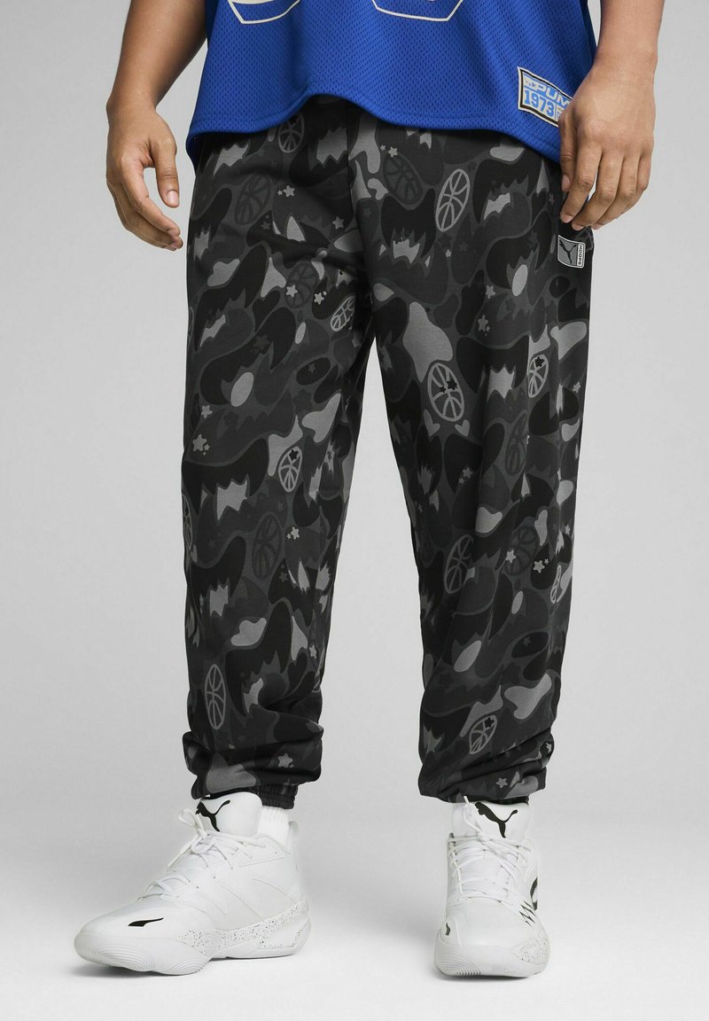 Sorte og grå camouflage sweatpants med forskellige mønstre, tætsiddende manchetter og en elastisk talje, parret med hvide sportssko.