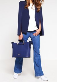 Námorně modrá kožená taška přes rameno se stříbrnými detaily, dvěma pevným uchy a prostorným designem. Kombinováno s volnými džíny a bílým topem.