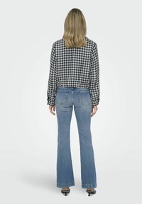 Cămașă croită cu model houndstooth alb-negru, asociată cu blugi evazați albaștri, dotată cu buzunare la spate și hem lungime la gleznă.