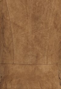 Gros plan d’un tissu en suède beige avec des coutures visibles et une surface douce texturée.
