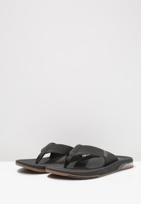 Zwarte teenslippers met gestructureerde synthetische banden, een gevormde voetbed en een bruine rubberen zool. Minimalistisch ontwerp, lichtgewicht constructie.