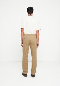 Beige trousers with a straight-leg fit, crafted from cotton. Features two rear pockets and subtle stitching details. Worn with a white t-shirt.