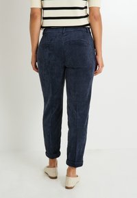 Pantalones de pana azul marino con un patrón de costura texturizado, que cuentan con dos bolsillos traseros y puños enrollados. Diseño sencillo y ajustado.
