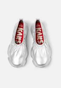 Metallic silver slip-on shoes with gathered top and rubber sole. Interior features red insole with white logo lettering. Smooth texture.