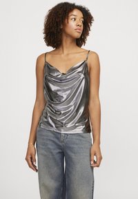 Top in raso argentato con design drappeggiato, spalline sottili regolabili e una texture morbida, abbinato a jeans di denim larghi.