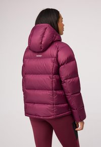 Bordowa kurtka puchowa z kapturem, o pikowanej fakturze i mocno zarysowanym fasonie. Logo marki umieszczone na górnej części pleców.