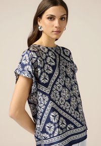 Navybluse mit floralem Muster und geometrischen Akzenten, kurzen Ärmeln, rundem Ausschnitt, glatter Textur und abgerundetem Saum.