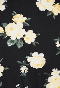 Svart tyg med stora gula rosor och små vita blommor, tillsammans med gröna löv, som visar ett blommönster på en strukturerad yta.