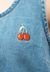 Κεντημένα κόκκινα κεράσια με πράσινα στελέχη σε μπλε τζιν ύφασμα, παρουσιάζοντας λεπτομερή ραφή και υφή.