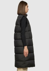 Gilet sans manches noir en doudoune avec un matelassage horizontal, un col montant et une silhouette droite, fabriqué à partir d'un matériau lisse et léger.