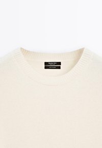 Cream-colored cashmere sweater with a round neckline, ribbed collar, and label displaying "Massimo Dutti" and "100% cashmere."