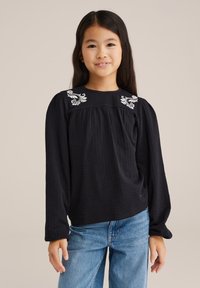 Mustha mustade pikkade varrukatega särk, millel on tekstuuriga kangas, ja õlgadel on valge lilleline tikand, koos helesiniste teksadega.